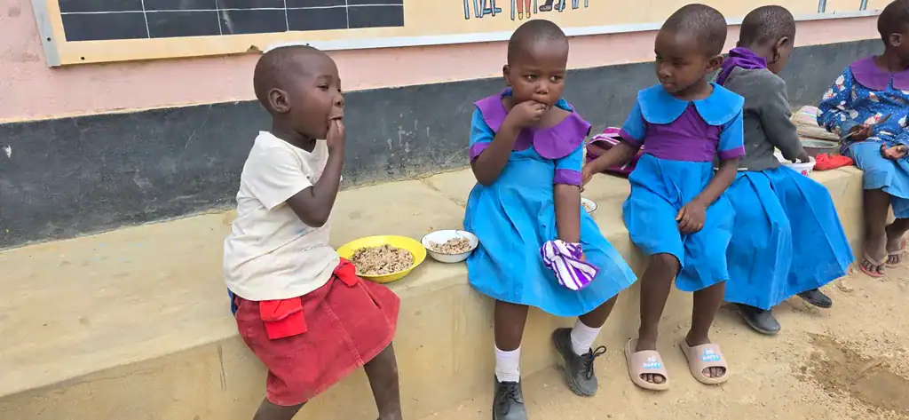 Primary school girls in Kilifi County, Kenya, seated outdoors eating a meal of rice, lentils and dried vegetables provided through Plan International's school feeding program.