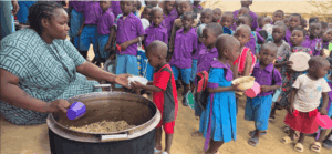 A teacher serves primary school children in Kilifi County, Kenya, as they queue to receive a meal of rice, lentils and dried vegetables through Plan International's school feeding program.