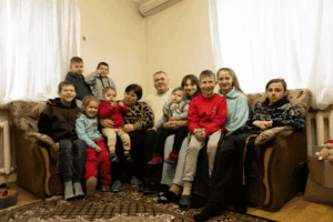 Foster parents Yuri and Nadia sit on a couch surrounded by their nine foster children of varying ages in their home in rural Ukraine.