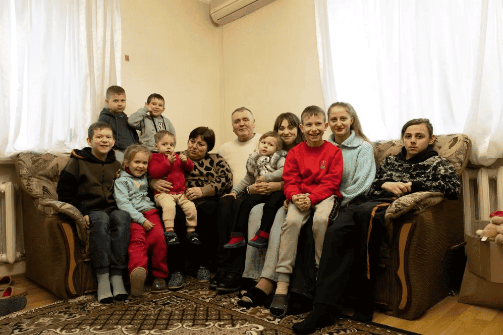 Foster parents Yuri and Nadia sit on a couch surrounded by their nine foster children of varying ages in their home in rural Ukraine.