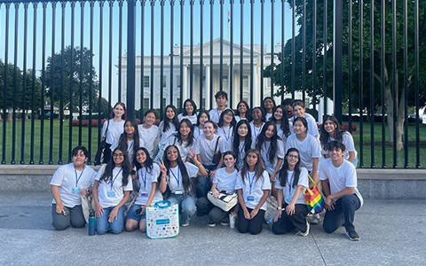 Group of Youth Leadership Academy members posing in front of a black metal fence with the White House visible in the background.